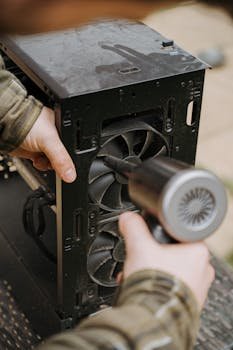 Person using air duster to clean a computer fan inside a desktop case.